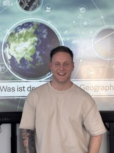 Abgebildet auf dem Bild ist Herr Döll, welcher vor einem unserer modernen Smartboards steht. Ein Foto von Herrn Döll nach dem Geographie Unterricht